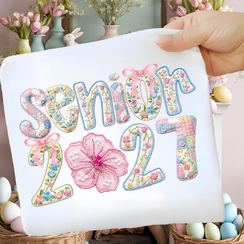 Puede incluir: Una tela blanca con la inscripci&oacute;n bordada "SENIOR 2021". Las letras y los n&uacute;meros est&aacute;n decorados con motivos florales, patchwork y lazos. Una gran flor rosa est&aacute; centrada debajo de la palabra "SENIOR".