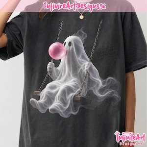 May include: A charcoal gray t-shirt featuring a graphic of a white ghost sitting on a wooden swing, blowing a large pink bubblegum bubble. The ghost has two dark oval eyes and is suspended by chains. The text InfiniteArtDesigns96 appears at the top.