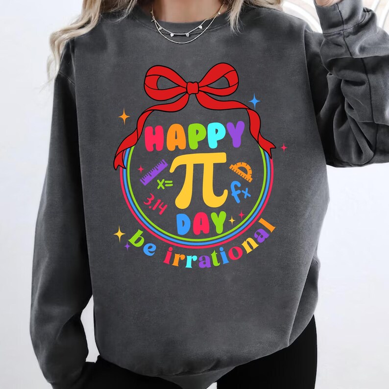 May include: A dark gray sweatshirt with a colorful graphic design that says "Happy Pi Day be irrational". The graphic features a large pi symbol with a red bow and math symbols around it.