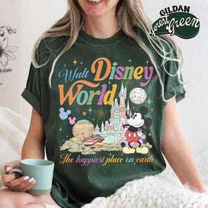 May include: Dark green t-shirt with a colorful "Walt Disney World" graphic featuring Mickey Mouse, a castle, and the phrase "The happiest place on earth." The shirt has a vintage, distressed look.