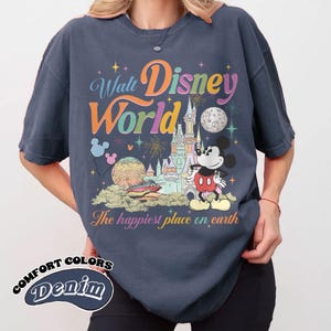 May include: Navy blue Comfort Colors denim t-shirt featuring a colorful Walt Disney World graphic. The design includes Mickey Mouse, a castle, fireworks, and the phrase "The happiest place on earth."