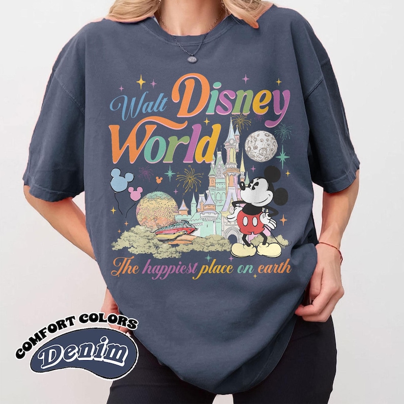 May include: Navy blue Comfort Colors denim t-shirt featuring a colorful Walt Disney World graphic. The design includes Mickey Mouse, a castle, fireworks, and the phrase "The happiest place on earth."