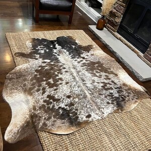 May include: A brown and white cowhide rug with a natural jute backing. The rug has a unique pattern of brown and white spots.