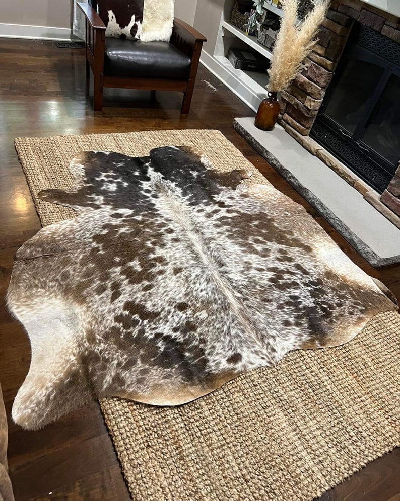 May include: A brown and white cowhide rug with a natural jute backing. The rug has a unique pattern of brown and white spots.
