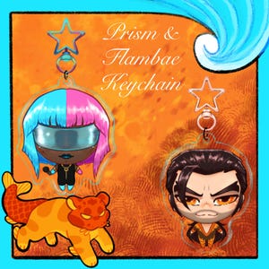 May include: Orange and blue background with the text "Prism & Flambae Keychain". The image features three keychains: a character with blue and pink hair, a character with black hair, and a cartoon tiger.
