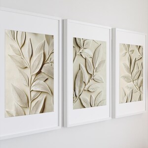 May include: Three white framed prints with a beige background and a raised embossed design of leaves in a light brown colour.