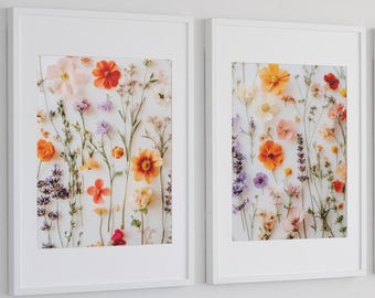 May include: Two framed floral art prints. Each print displays a collection of colourful flowers, including orange, yellow, pink, and purple blooms, arranged against a white background. The frames are white.
