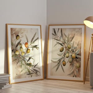 May include: Two framed watercolour prints of olive branches with green and orange olives. The artwork has a neutral colour palette with a light brown wooden frame. The prints are leaning against a white wall.