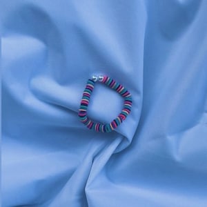 May include: A colorful striped bracelet with silver beads on a light blue background.