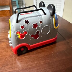 K&ouml;nnte beinhalten: Ein graues und rotes Spielzeugfahrzeug mit schwarzen Griffen und Mickey Mouse Ohren. Das Fahrzeug hat Stern- und Mickey Mouse-Kopf-Ausschnitte sowie gelbe und blaue Akzente. Die R&auml;der sind schwarz und rot.