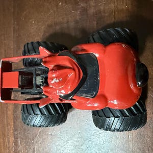 May include: A red and black toy monster truck with large black tires. The truck has a detailed design with a red body and black accents. The tires are thick and have a deep tread pattern.