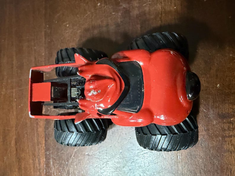 May include: A red and black toy monster truck with large black tires. The truck has a detailed design with a red body and black accents. The tires are thick and have a deep tread pattern.