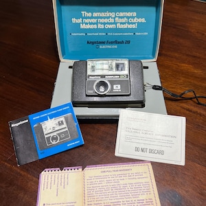 May include: A vintage Keystone Everflash 20 camera in its original box, with the text "The amazing camera that never needs flash cubes. Makes its own flashes!" Also included are manuals and warranty information.