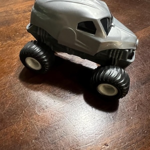 May include: A grey toy monster truck with black wheels. The truck has a skull-like design on the front.