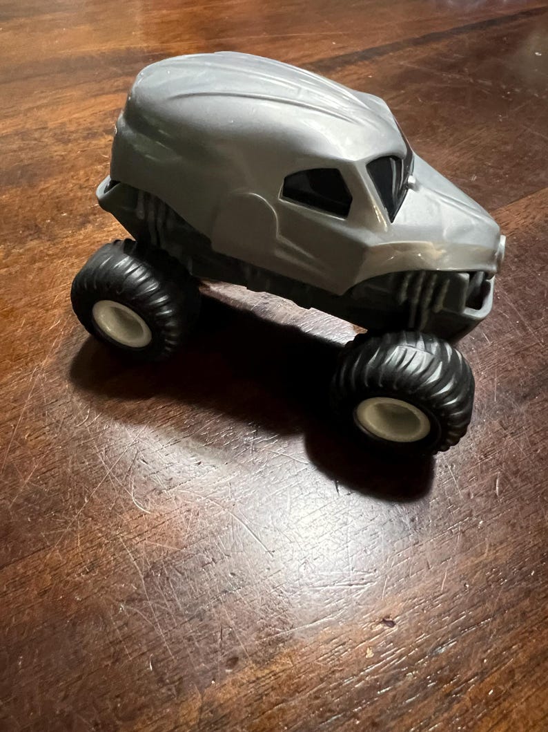 May include: A grey toy monster truck with black wheels. The truck has a skull-like design on the front.
