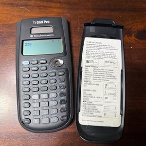May include: A black TI-36X Pro calculator with a display showing "23". The calculator has numerous buttons for scientific and mathematical functions. The open battery cover displays instructions.