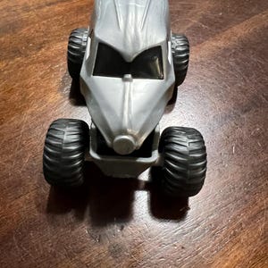 May include: A silver toy car with black tyres. The car has a futuristic design with a rounded body and a large windscreen.