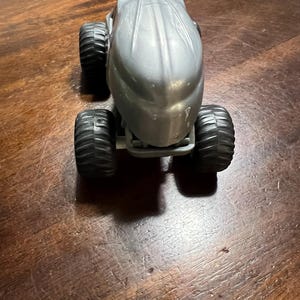May include: A silver toy monster truck with large black wheels. The truck has a unique, streamlined design.