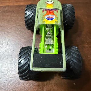 Puede incluir: Un juguete de cami&oacute;n monstruo verde con neum&aacute;ticos negros grandes. El cami&oacute;n tiene un marco verde y un motor detallado. La parte delantera del cami&oacute;n presenta un logotipo con el texto "Lucas Oil Products Inc."