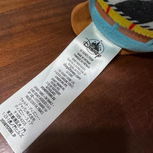 May include: A close-up of a white tag with the Disney logo and text. The tag reads "MADE IN VIETNAM" and includes the shopDisney.com website address. The tag also lists the Disney Store Ltd. address in London.
