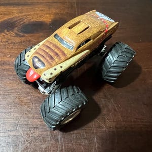 May include: A brown and tan monster truck toy with large black tyres. The truck has a detailed design with a red accent on the front and a textured pattern on the body. The tyres are approximately 7.6 cm in diameter.