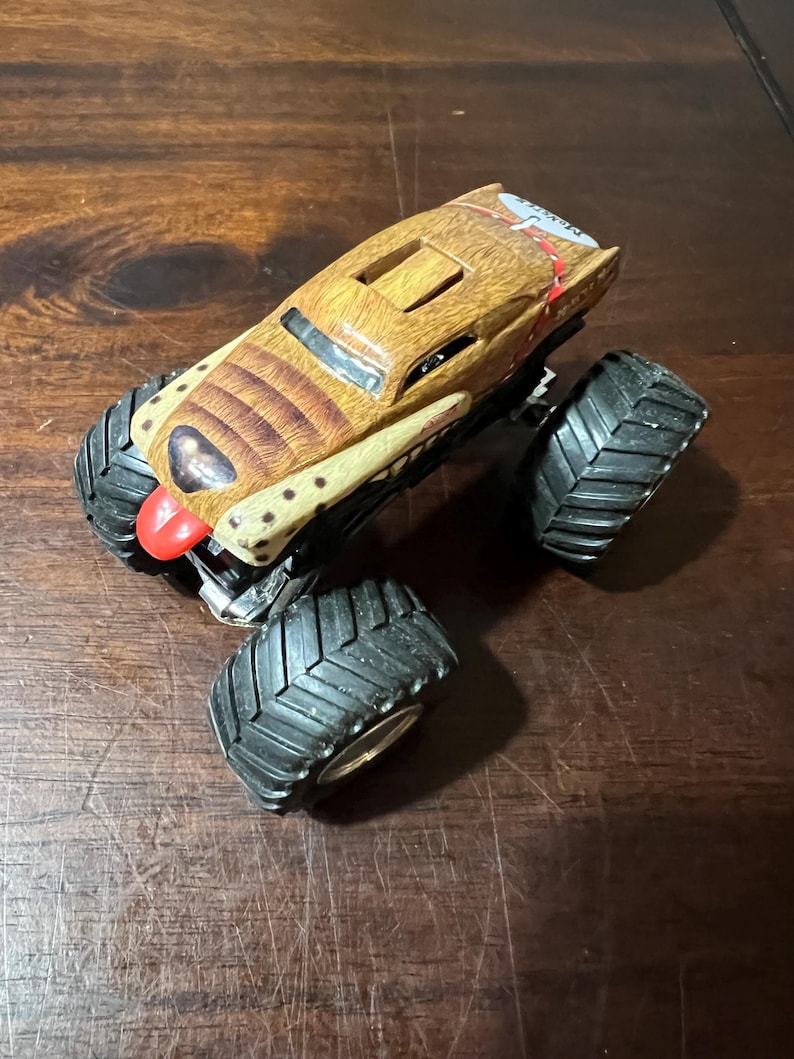 May include: A brown and tan monster truck toy with large black tyres. The truck has a detailed design with a red accent on the front and a textured pattern on the body. The tyres are approximately 7.6 cm in diameter.