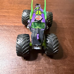 May include: A black and purple toy monster truck with large black tyres. The truck has green accents and the word "BAKUGAN" is visible on the front. The truck is sitting on a brown surface.