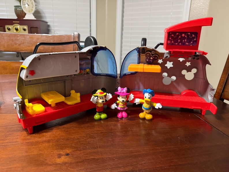 K&ouml;nnte beinhalten: Ein rotes, graues und gelbes Spielzeug-Spielset mit Mickey Mouse, Minnie Mouse und Donald Duck Figuren. Das Spielset hat eine rote Basis, graue W&auml;nde und einen roten Deckel mit einem Bildschirm. Die Figuren tragen bunte Outfits.