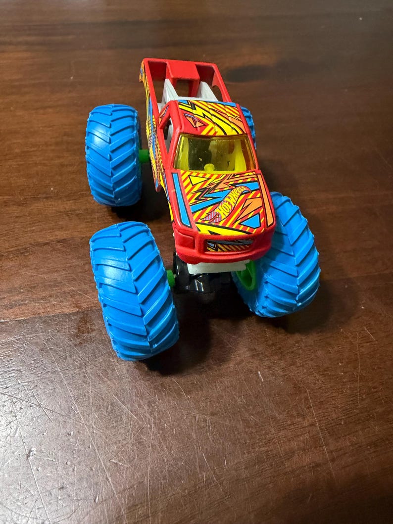 Puede incluir: Un juguete de cami&oacute;n monstruo Hot Wheels rojo y amarillo con neum&aacute;ticos azules. El cami&oacute;n tiene un dise&ntilde;o detallado con el logotipo de Hot Wheels y un parabrisas amarillo. Los grandes neum&aacute;ticos azules tienen un dibujo profundo.