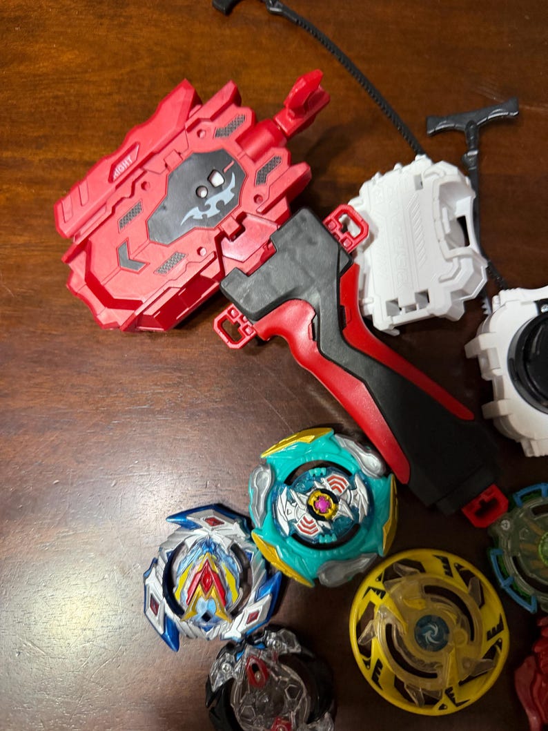 May include: A collection of colorful spinning top toys and launchers. The tops feature various designs with blue, yellow, green, and red accents. Launchers are red, black, and white. The toys are designed for competitive play.