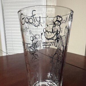 May include: A clear glass tumbler featuring black line art sketches of the character Goofy. The design includes the text Goofy and instructions that read SNOUT TILTS UPWARD A LITTLE, along with various technical drawing annotations and character poses.