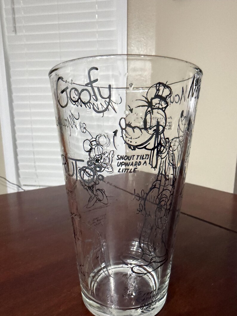 May include: A clear glass tumbler featuring black line art sketches of the character Goofy. The design includes the text Goofy and instructions that read SNOUT TILTS UPWARD A LITTLE, along with various technical drawing annotations and character poses.