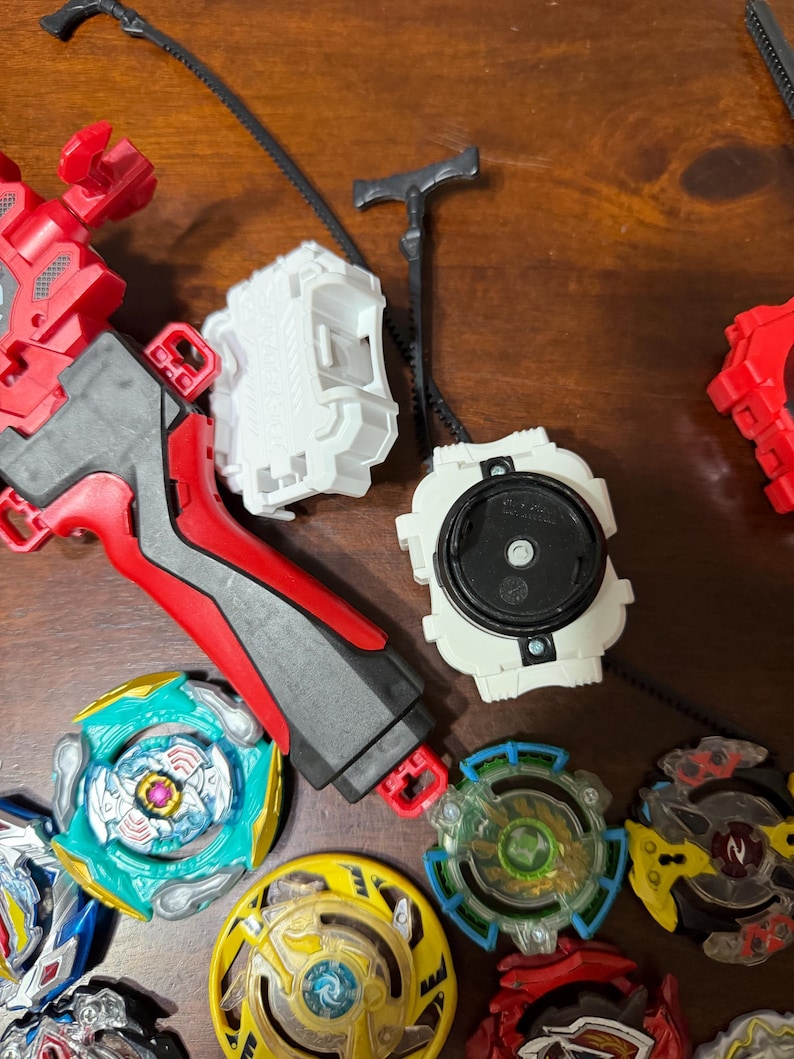 May include: A collection of colorful spinning top toys and launchers. The tops feature various designs with blue, green, yellow, and red accents. Launchers are red, white, and black. The toys are designed for competitive play.