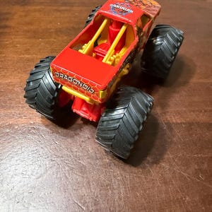 K&ouml;nnte beinhalten: Ein roter und gelber Spielzeug-Monstertruck mit gro&szlig;en schwarzen Reifen. Der Truck tr&auml;gt die Aufschrift "DRAGONOID" an der Seite und "BAKUGAN" oben.