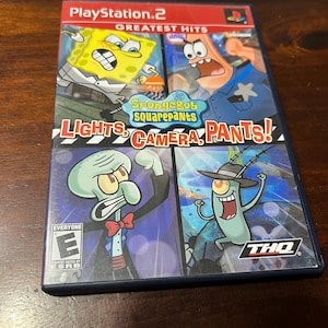 Puede incluir: Caja de videojuego de PlayStation 2 para "Bob Esponja: Luces, Cámara, Pantalones!" con los personajes de dibujos animados Bob Esponja, Patricio, Calamardo y Plankton. La caja está etiquetada como "GREATEST HITS" y clasificada "E" para todos por ESRB.