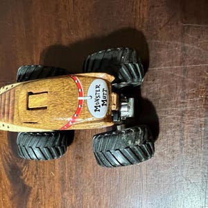 May include: A toy Monster Mutt monster truck with a brown body and black tyres. The truck has a red and white stripe design and the words "Monster Mutt" on the side.