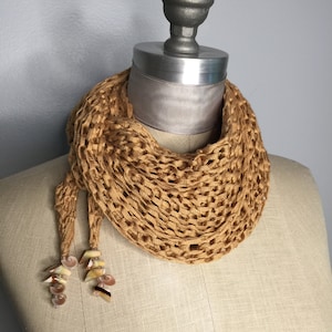 Puede incluir: Una bufanda de crochet de color beige con detalles de conchas. La bufanda se muestra en un maniquí.