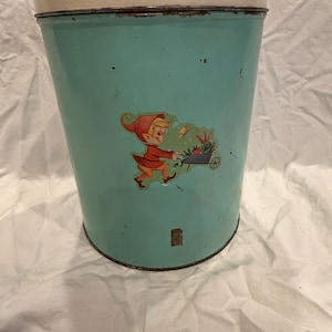 Può includere: Contenitore vintage in metallo turchese con coperchio color crema. Il contenitore cilindrico presenta un'illustrazione colorata di un elfo dei cartoni animati che spinge una carriola piena di verdure. Il contenitore mostra segni di usura.