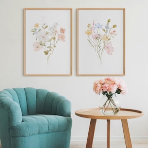 以下が含まれることがあります： 淡い木製のフレームに入った2つの花の水彩画プリントが、ターコイズのアームチェアの上に飾られています。丸い木製のサイドテーブルには、ピンクの花が入ったガラスの花瓶が置かれています。
