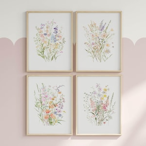 May include: Set of four framed prints featuring watercolour illustrations of delicate wildflowers in shades of pink, purple, and yellow. The prints are arranged in a grid pattern on a light pink wall.