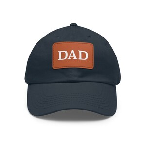 May include: A navy blue baseball cap with a brown leather patch that says "DAD" in white letters.