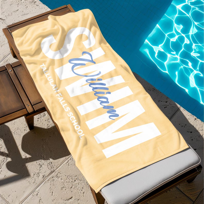 May include: A yellow beach towel with the name "William" in white block letters and a cursive blue "William" overlay. The towel is on a wooden lounge chair next to a pool. The text "Tallulah Falls School" is also visible.