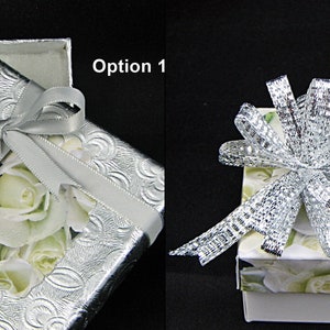 May include: Two gift boxes with different ribbon styles. The box on the left has a silver ribbon with a bow and a white rose pattern. The box on the right has a silver mesh ribbon with a bow and a white rose pattern.