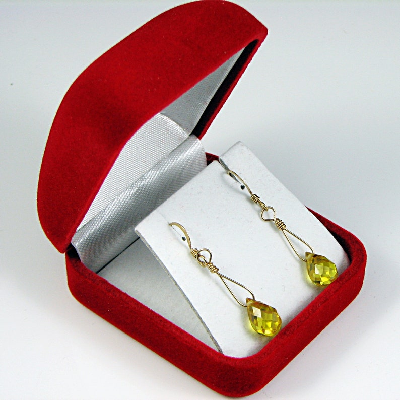 May include: A pair of gold earrings with teardrop-shaped yellow gemstones, displayed in a red velvet jewelry box.