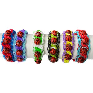 May include: Six colorful rubber band bracelets with basketball charms. The bracelets are made with different colored rubber bands and feature a basketball charm on each link.