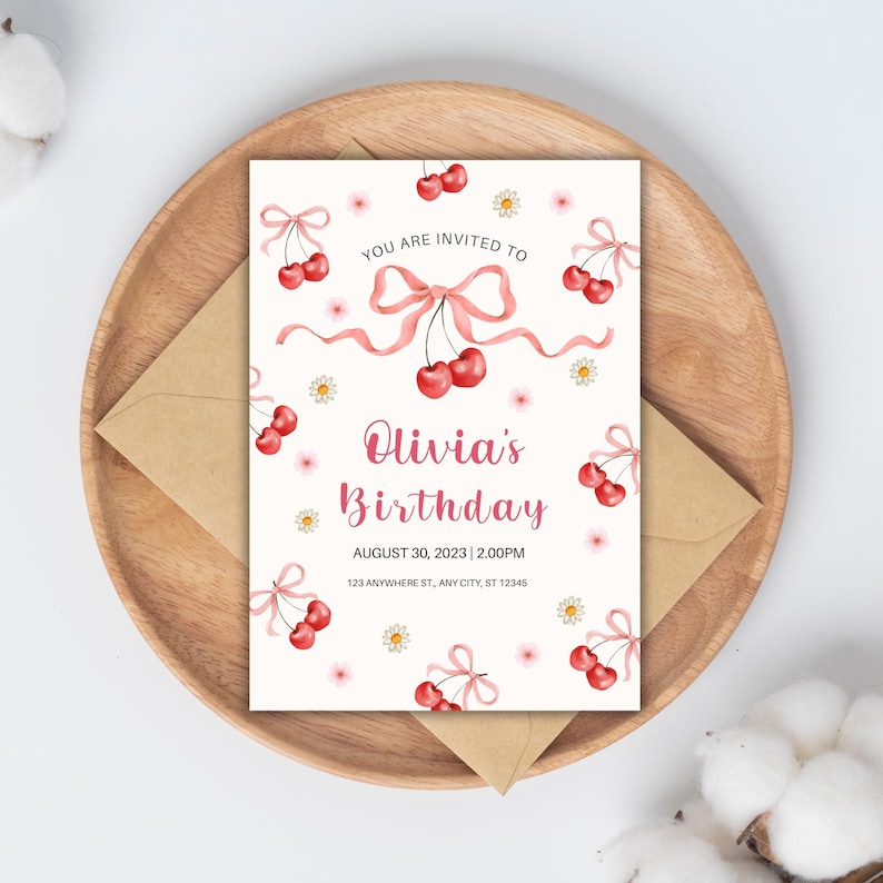 Puede incluir: Una invitaci&oacute;n de cumplea&ntilde;os con tema de cerezas. La invitaci&oacute;n presenta cerezas rojas, lazos rosas y peque&ntilde;as flores blancas sobre un fondo crema. El texto dice "You are invited to Olivia's Birthday" con la fecha y hora.