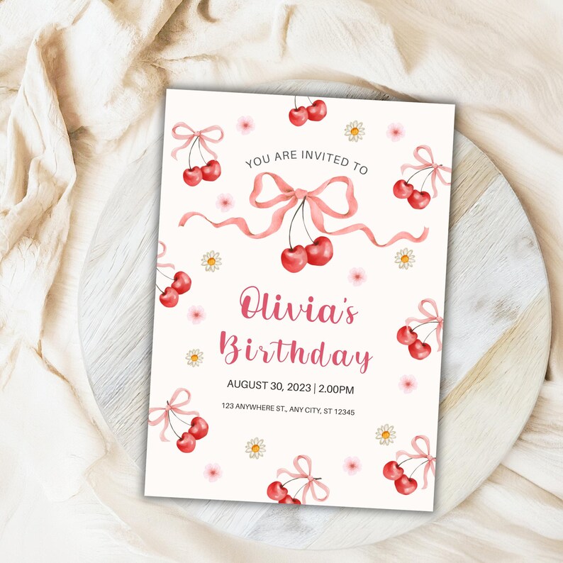 Puede incluir: Una invitaci&oacute;n de cumplea&ntilde;os color crema con cerezas en acuarela y lazos rosas. El texto dice "YOU ARE INVITED TO Olivia's Birthday AUGUST 30, 2023 | 2.00PM 123 ANYWHERE ST, ANY CITY, ST 12345". Peque&ntilde;as margaritas salpican el dise&ntilde;o.