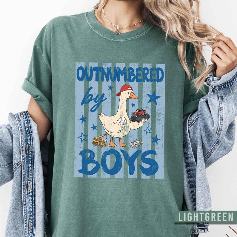 Peut inclure: T-shirt vert clair avec un motif &laquo;&nbsp;OUTNUMBERED by BOYS&nbsp;&raquo;. Le motif repr&eacute;sente une oie de dessin anim&eacute; portant une casquette rouge, tenant une balle de baseball et un camion jouet. Des &eacute;toiles et des rayures bleues compl&egrave;tent le motif.