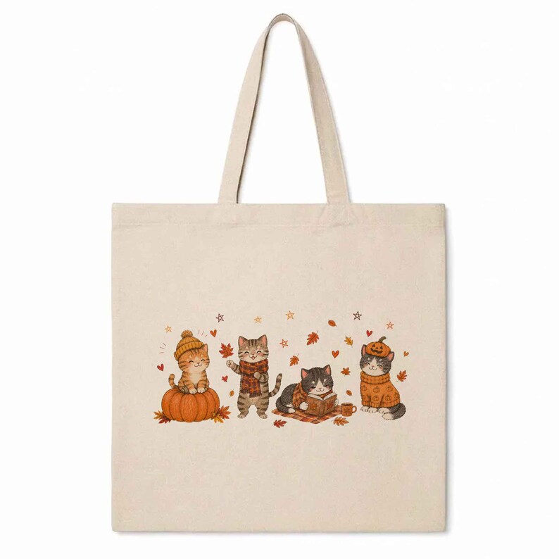 May include: A beige canvas tote bag featuring a printed illustration of four cats in autumn-themed attire. One cat sits on a pumpkin, another wears a scarf, one reads a book, and the last wears a pumpkin hat, all surrounded by falling leaves.