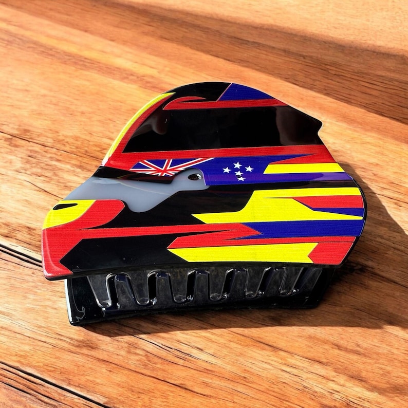 May include: A black hair claw clip with a colorful design featuring red, yellow, blue, and black geometric shapes. The clip also includes a small Union Jack and a constellation of stars.